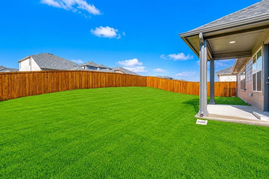 Expansive backyard with a large lawn area, stained wood privacy fence, and a covered patio featuring recessed lighting
