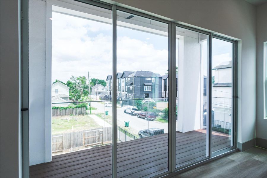 Representative Balcony View (Design selections and colors may vary): The balcony features earth-toned Trex® composite decking and is ideal for morning coffee or evening relaxation. It is accessible via the glass sliding doors that connect the living area in the middle level.