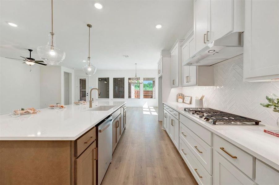 Open-concept kitchen featuring an expansive island with a built-in sink, stainless steel appliances, and pendant lighting Open-concept kitchen featuring an expansive island with a built-in sink, stainless steel appliances, and pendant lighting