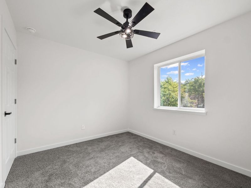 Room with light grey carpet flooring, white walls, and a modern black ceiling fan with integrated lighting