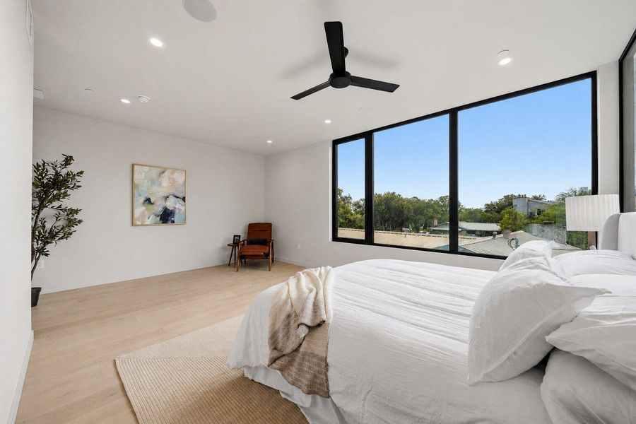 A tranquil bedroom retreat features a ceiling fan, recessed lighting, and a panoramic window framing a serene view. A tranquil bedroom retreat features a ceiling fan, recessed lighting, and a panoramic window framing a serene view.