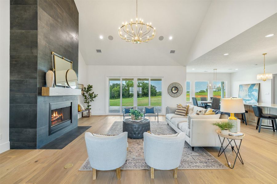 Living room featuring a chandelier, light wood finished floors, recessed lighting, high vaulted ceiling, and a tiled fireplace