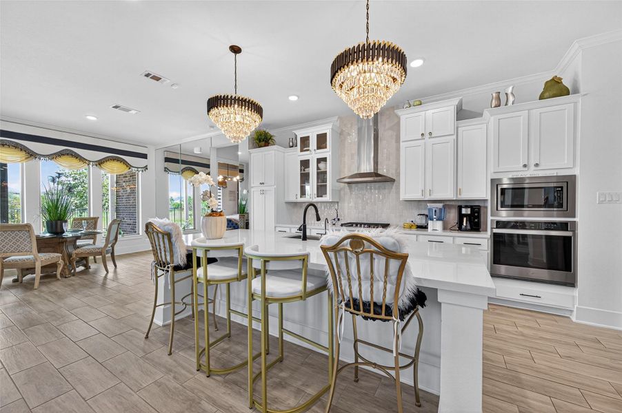 This modern kitchen features a bright, open layout with a large island, elegant chandeliers, and white cabinetry. It includes stainless steel appliances and a cozy dining area with large windows providing ample natural light. This modern kitchen features a bright, open layout with a large island, elegant chandeliers, and white cabinetry. It includes stainless steel appliances and a cozy dining area with large windows providing ample natural light.