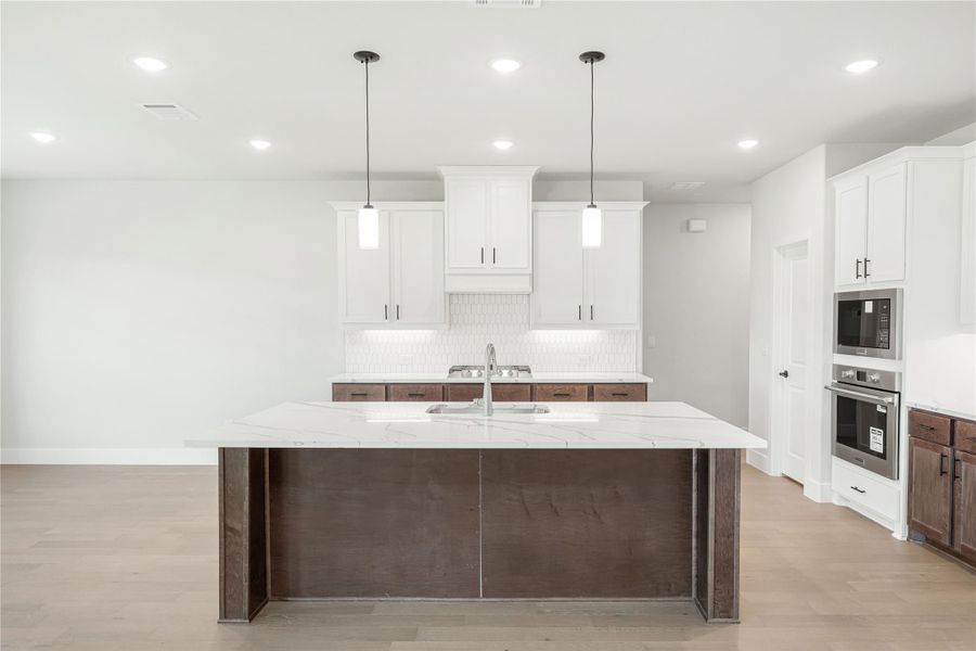 Kitchen with large island, quartz countertop, white cabinets, dark wood accents, and pendant lights above sink Kitchen with large island, quartz countertop, white cabinets, dark wood accents, and pendant lights above sink