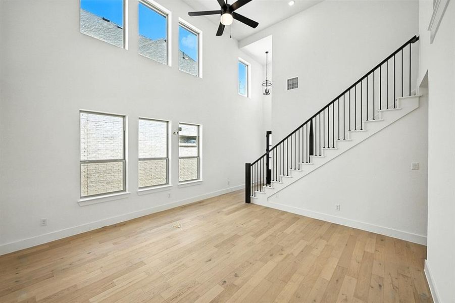 Unfurnished living room with stairs, light wood-type flooring, a ceiling fan, and a high ceiling Unfurnished living room with stairs, light wood-type flooring, a ceiling fan, and a high ceiling