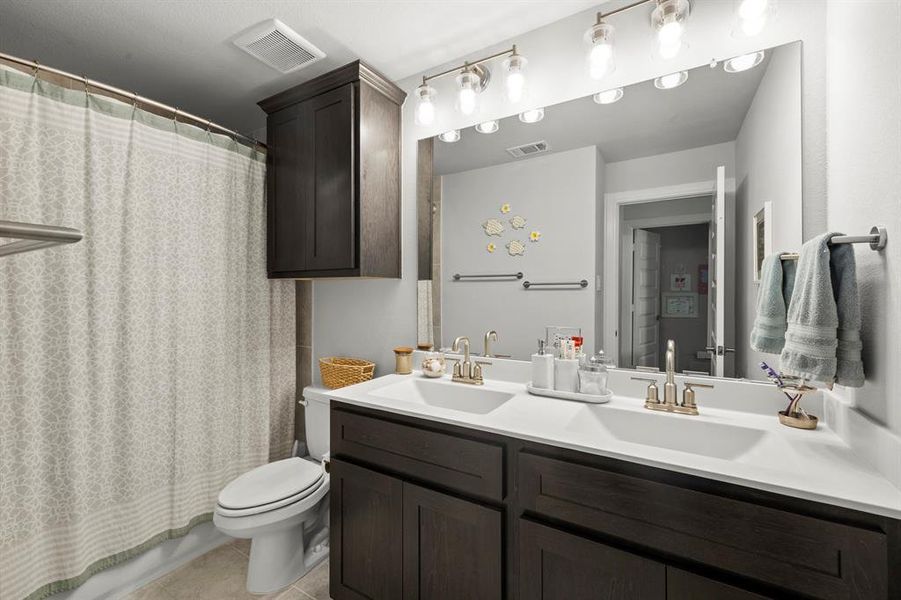 Bathroom featuring double vanity, light tile patterned floors, and shower / bath combo Bathroom featuring double vanity, light tile patterned floors, and shower / bath combo