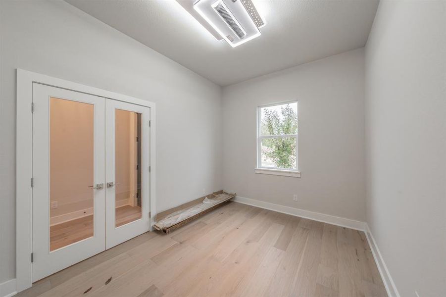 Empty room featuring french doors, light wood-type flooring, and cooling unit