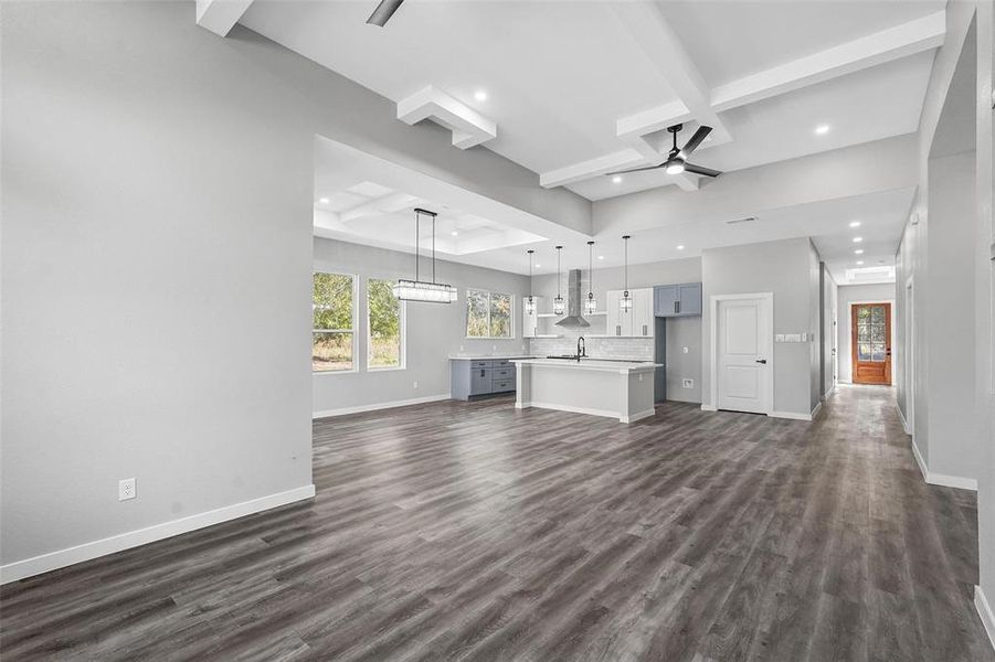 Unfurnished living room with dark wood-type flooring, coffered ceiling, ceiling fan, and beam ceiling