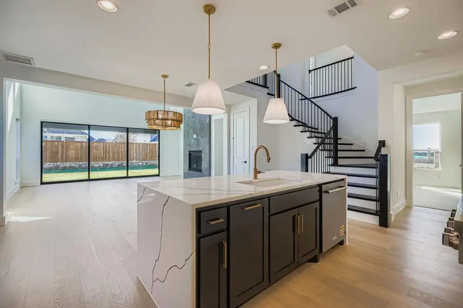 Kitchen with dark cabinetry, decorative light fixtures, light wood-style floors, recessed lighting, and light stone counters