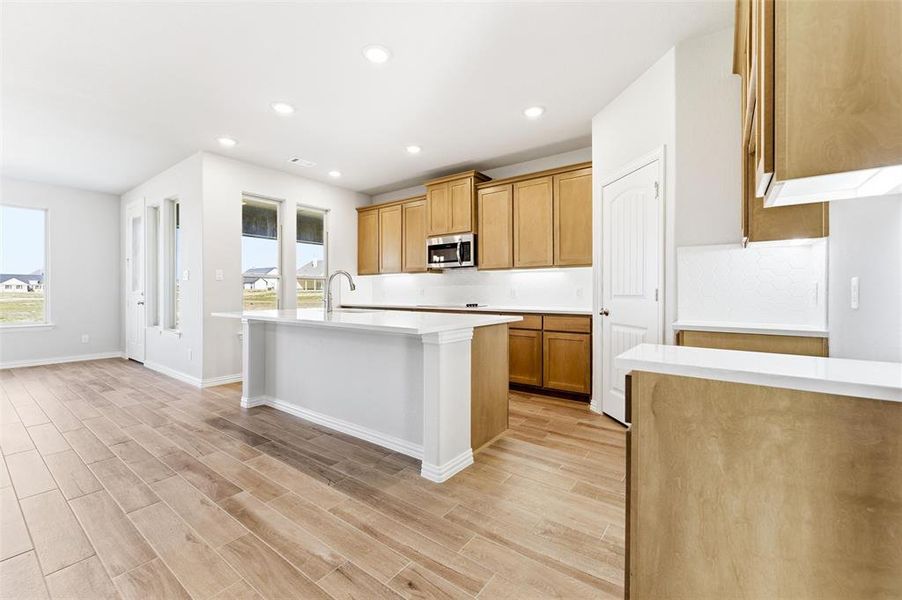 Kitchen with an island with sink, recessed lighting, wood tiled floors, and brown cabinets