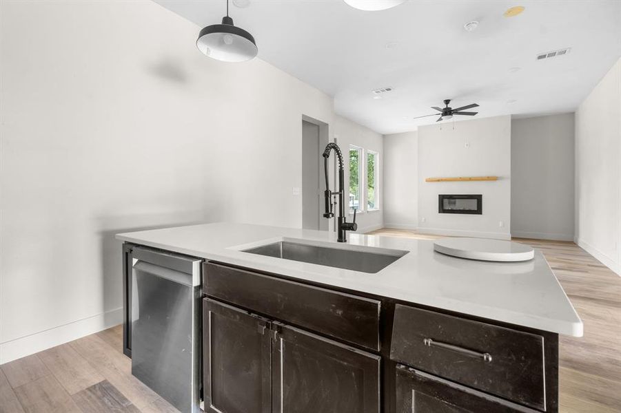 Kitchen featuring light wood-style flooring, dark brown cabinetry, open floor plan, a kitchen island with sink, and a glass covered fireplace