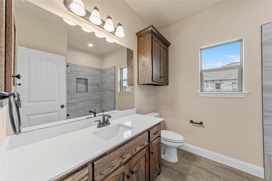 Bathroom with baseboards, wood finished floors, vanity, a tile shower, and toilet