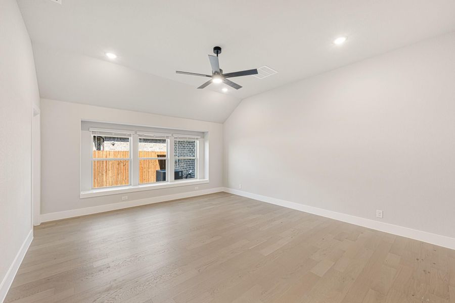 Empty room with vaulted ceiling, ceiling fan, hardwood floors, and a wide window overlooking a backyard fence. Empty room with vaulted ceiling, ceiling fan, hardwood floors, and a wide window overlooking a backyard fence.