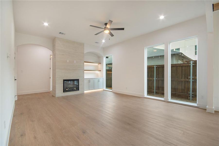 Unfurnished living room featuring light wood finished floors, ceiling fan, a tile fireplace, built in shelves, and recessed lighting