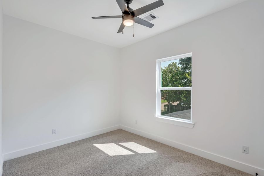 Third upstairs bedroom featuring soft carpet flooring, ceiling fan, and large window providing natural light.
