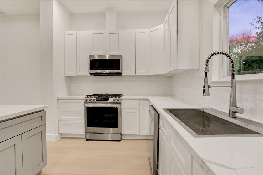 Sleek kitchen design with gas range, electric oven, Samsung brand consistent for microwave, stove, and dishwasher, custom sink faucet, and spacious countertops.