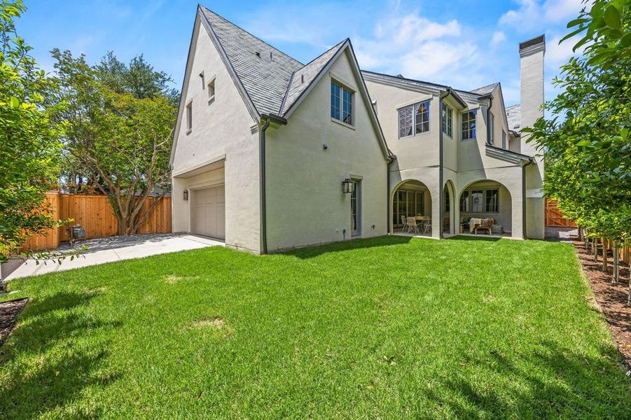 Expansive rear exterior featuring a stucco facade, multiple arched patio entries, a covered patio area, a prominent chimney, and a two-car garage with a concrete driveway Expansive rear exterior featuring a stucco facade, multiple arched patio entries, a covered patio area, a prominent chimney, and a two-car garage with a concrete driveway