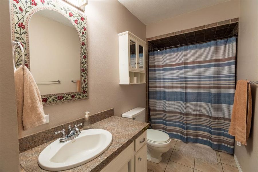 Bathroom with a shower with curtain, vanity, light tile patterned floors, and a textured wall Bathroom with a shower with curtain, vanity, light tile patterned floors, and a textured wall
