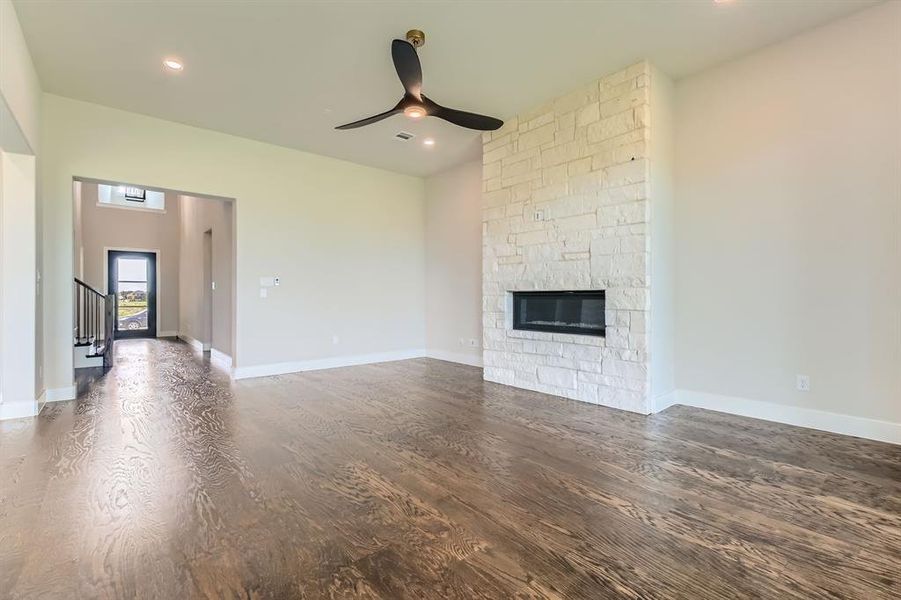 Unfurnished living room with a ceiling fan, wood finished floors, a stone fireplace, recessed lighting, and stairs Unfurnished living room with a ceiling fan, wood finished floors, a stone fireplace, recessed lighting, and stairs