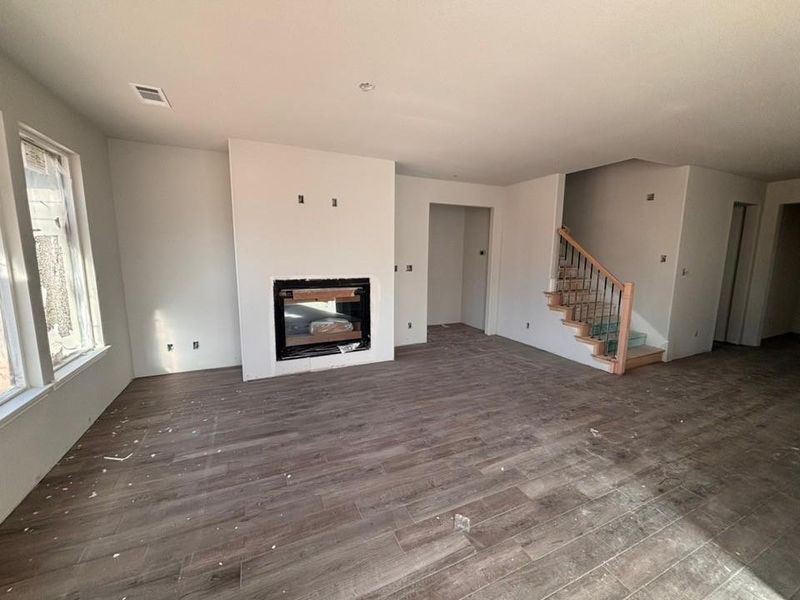 Unfurnished living room featuring a glass covered fireplace, stairway, and dark wood-type flooring Unfurnished living room featuring a glass covered fireplace, stairway, and dark wood-type flooring