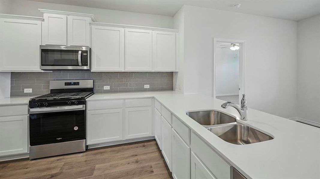 Kitchen featuring stainless steel appliances, white cabinetry, light wood finished floors, tasteful backsplash, and light stone countertops Kitchen featuring stainless steel appliances, white cabinetry, light wood finished floors, tasteful backsplash, and light stone countertops