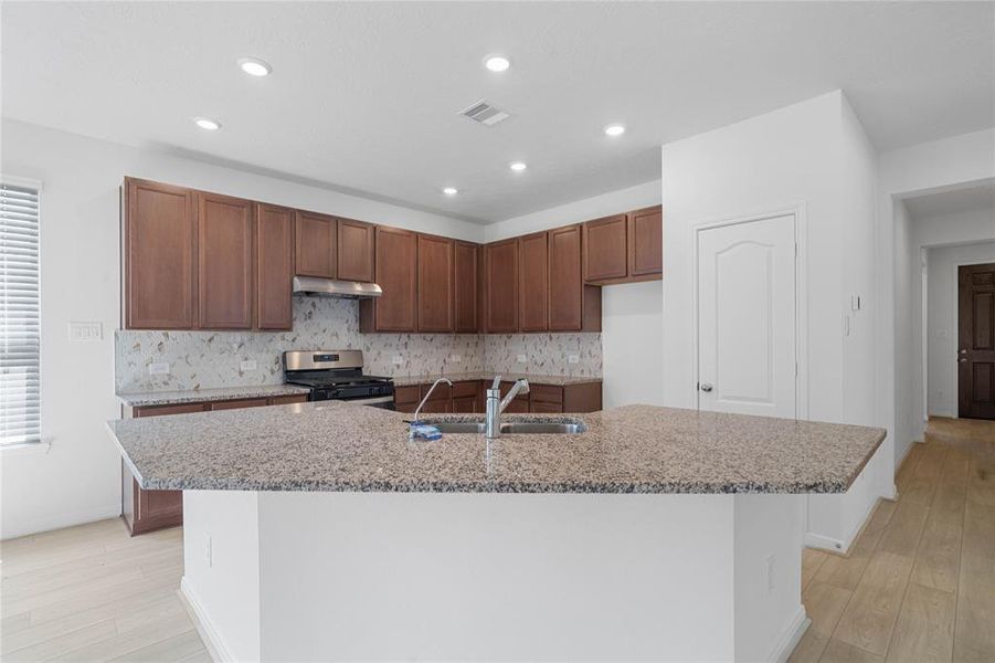 This spacious kitchen features high ceilings, stained wood cabinets, granite countertops, SS appliances, modern tile backsplash, recessed lighting, huge granite kitchen island with large single sink and space for breakfast bar, and a pantry all overlooking your huge family room.