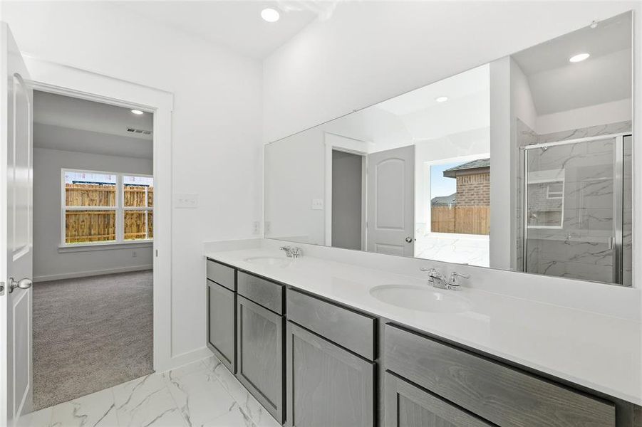 Full bathroom with double vanity, light marble finish floors, and a marble finish shower