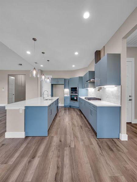 Kitchen with hanging light fixtures, an island with sink, light hardwood / wood-style flooring, sink, and blue cabinets