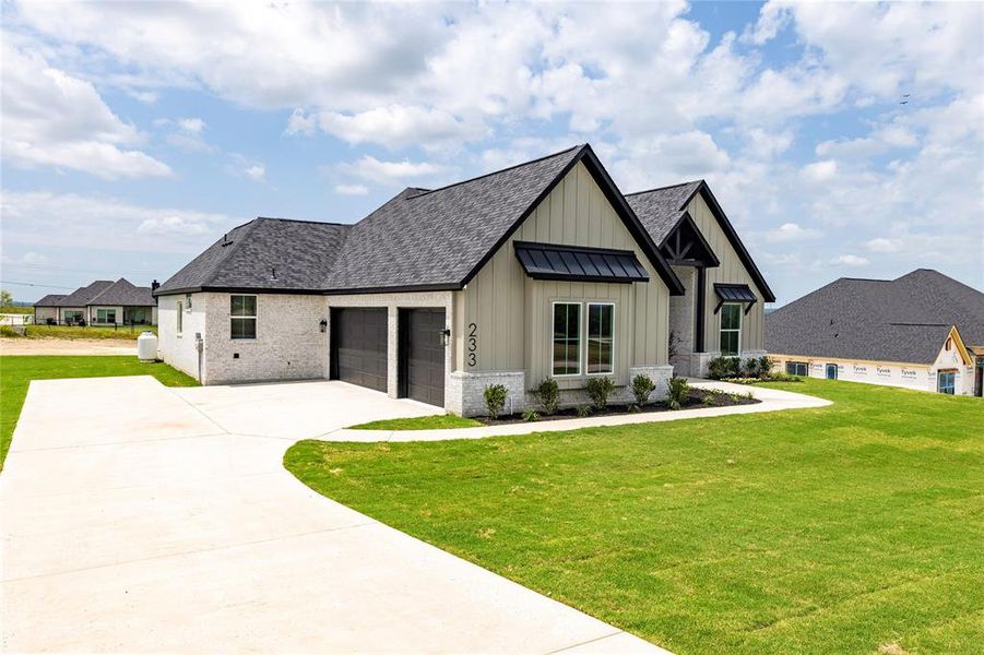 Modern farmhouse featuring board and batten siding, brick siding, a front yard, and concrete driveway