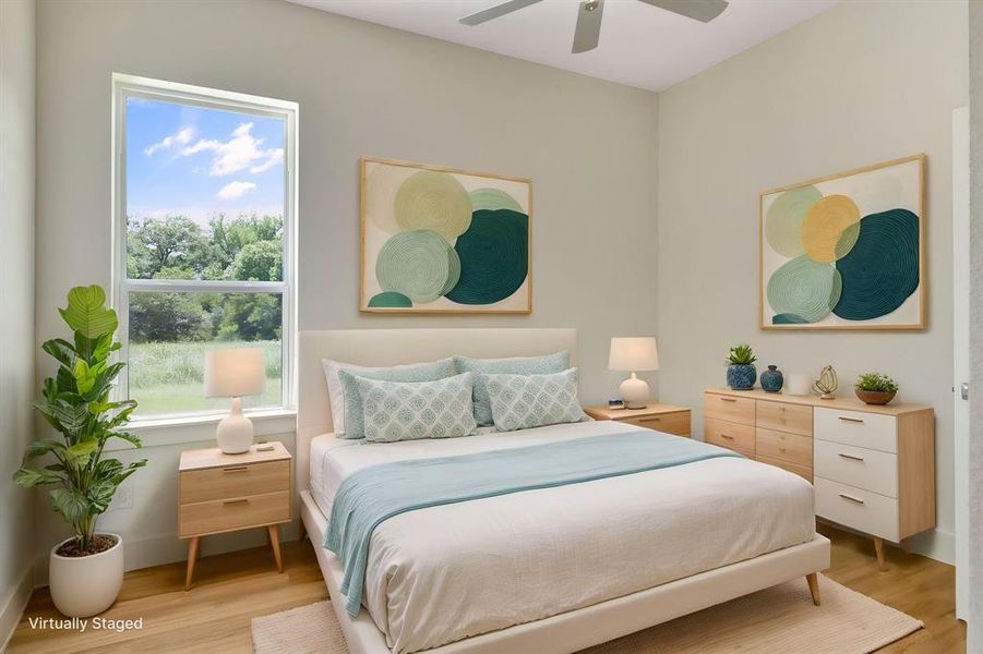 Spacious bedroom featuring light wood-finish flooring, a large window offering expansive outdoor scenery, a ceiling fan, and ample wall space Spacious bedroom featuring light wood-finish flooring, a large window offering expansive outdoor scenery, a ceiling fan, and ample wall space