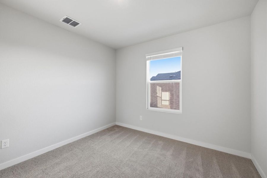 A well-lit bedroom features plush carpeting and a window offering views of the neighborhood.