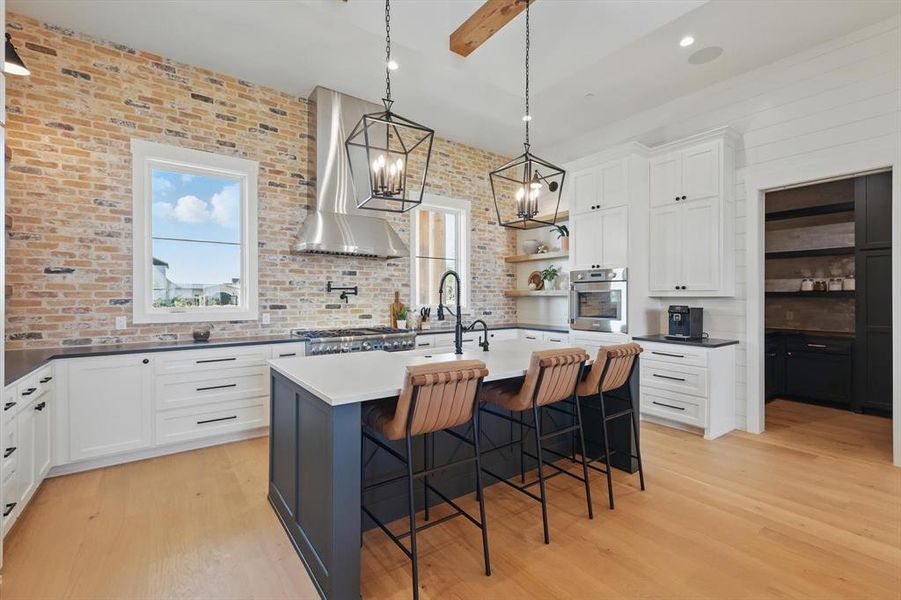 Kitchen featuring wall chimney range hood, oven, light wood-style flooring, a breakfast bar area, and a chandelier Kitchen featuring wall chimney range hood, oven, light wood-style flooring, a breakfast bar area, and a chandelier