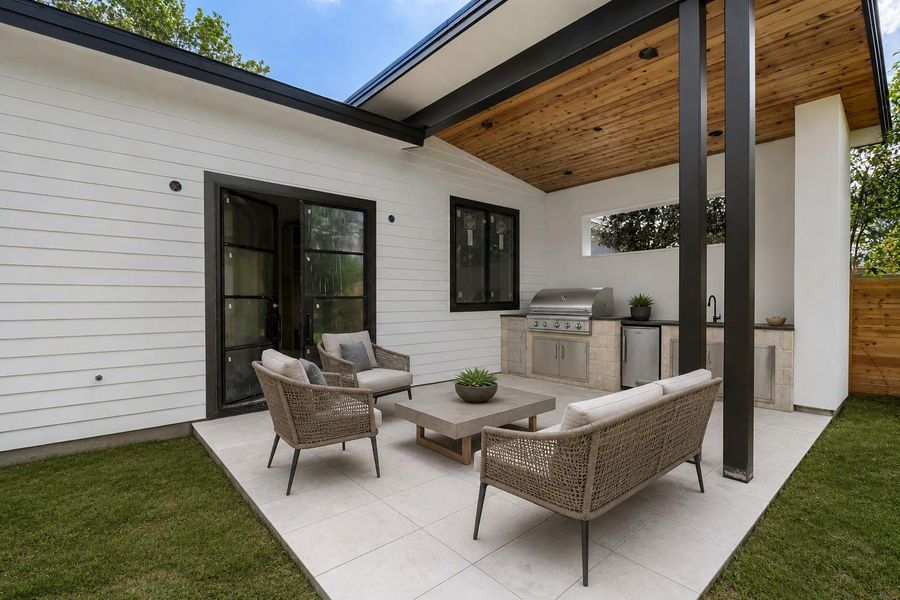 Outdoor patio featuring a built-in kitchen with stainless steel grill and sink, light-colored tile flooring, and a wood-paneled ceiling
