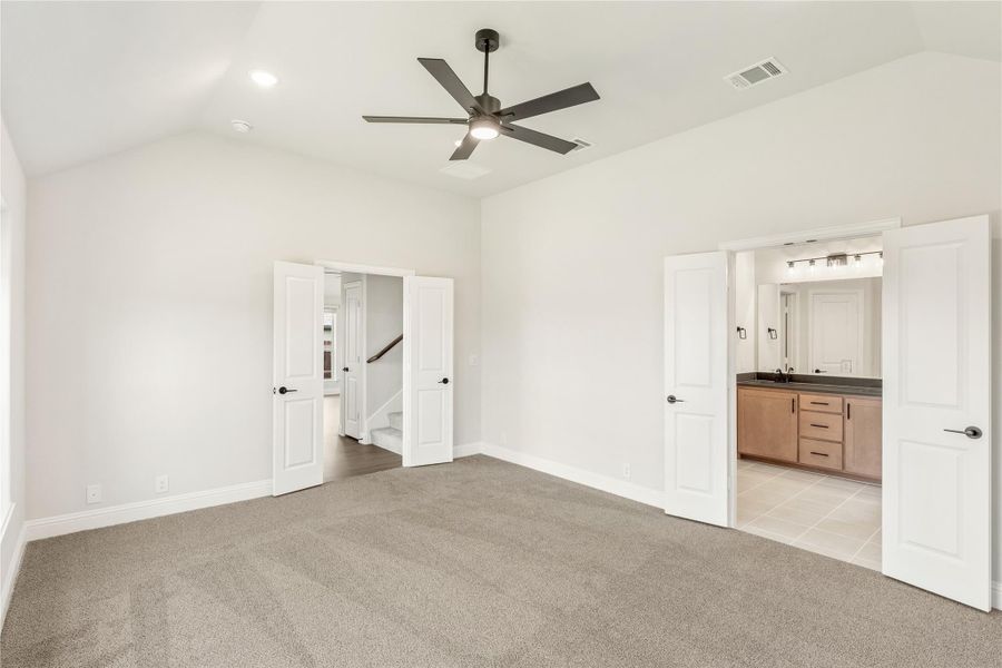 Spacious master bedroom with vaulted ceiling, ceiling fan, carpet flooring, and ensuite bathroom visible through open door. Spacious master bedroom with vaulted ceiling, ceiling fan, carpet flooring, and ensuite bathroom visible through open door.