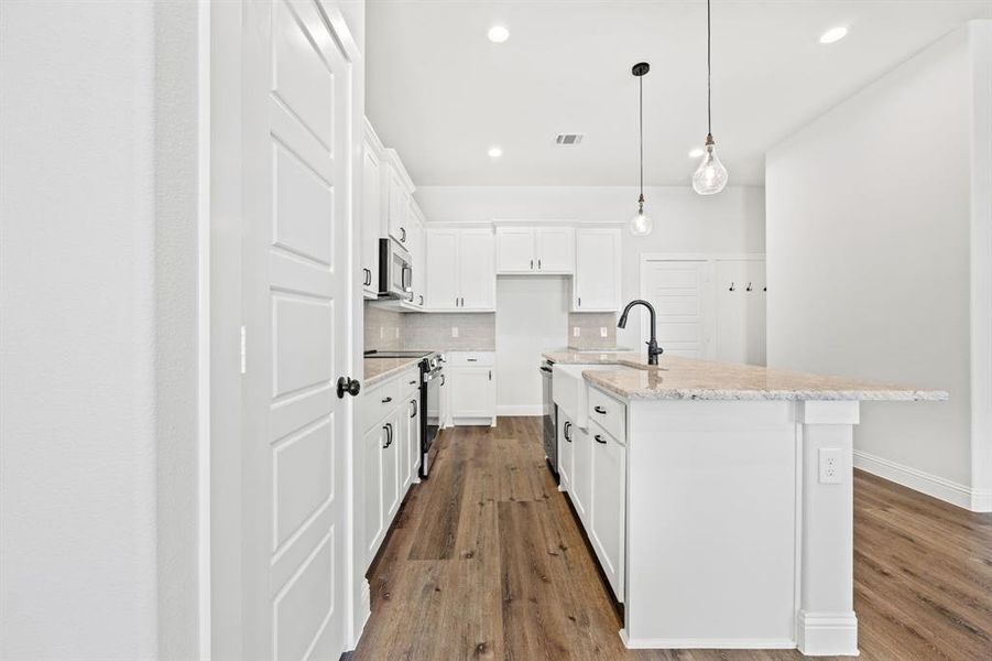 Kitchen with stainless steel appliances, white cabinetry, tasteful backsplash, an island with sink, and wood-type flooring