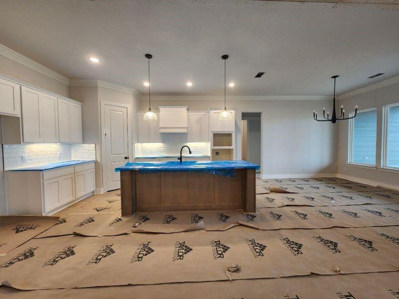 Kitchen with crown molding, white cabinets, an island with sink, pendant lighting, and a chandelier