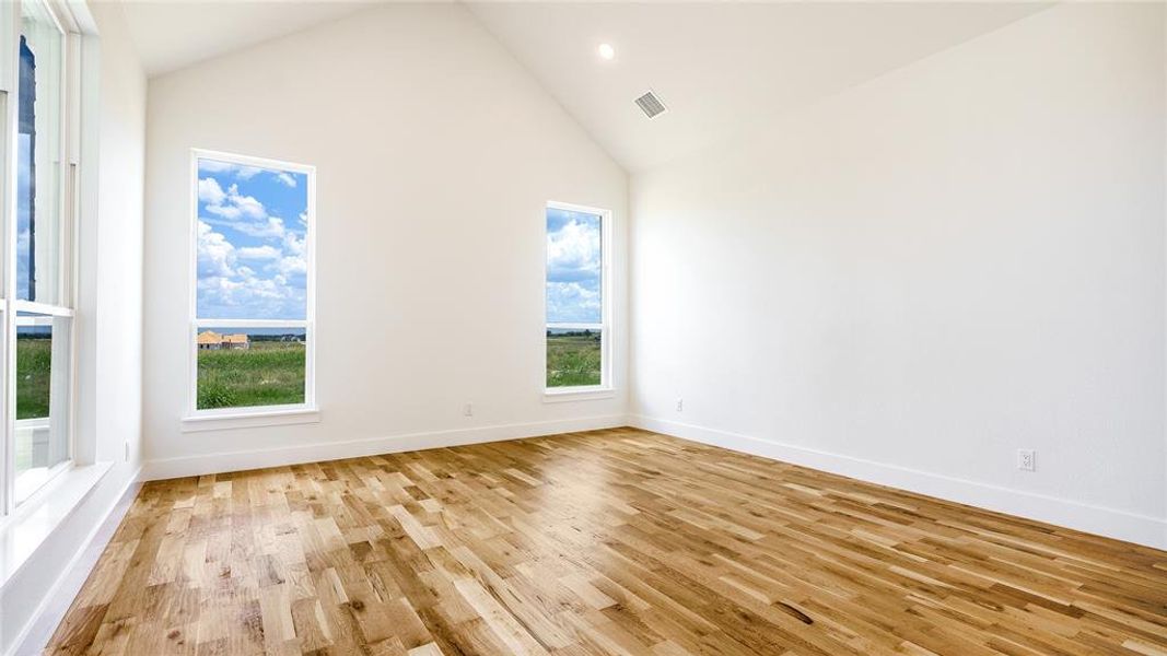 Empty room with high vaulted ceiling and light wood-type flooring