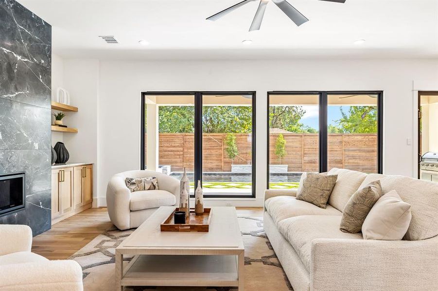 Living area featuring plenty of natural light, a high end fireplace, light wood-style flooring, recessed lighting, and a ceiling fan Living area featuring plenty of natural light, a high end fireplace, light wood-style flooring, recessed lighting, and a ceiling fan