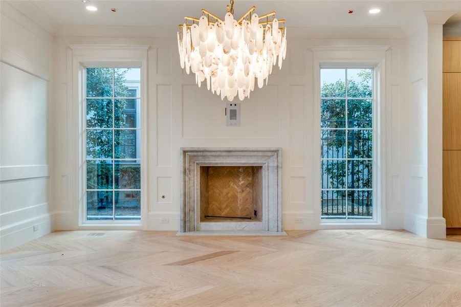 Unfurnished living room featuring an inviting chandelier, a healthy amount of sunlight, ornamental molding, and light parquet floors