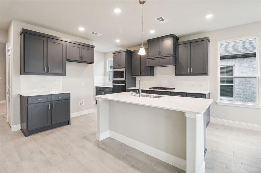 Kitchen featuring sink, hanging light fixtures, an island with sink, decorative backsplash, and appliances with stainless steel finishes