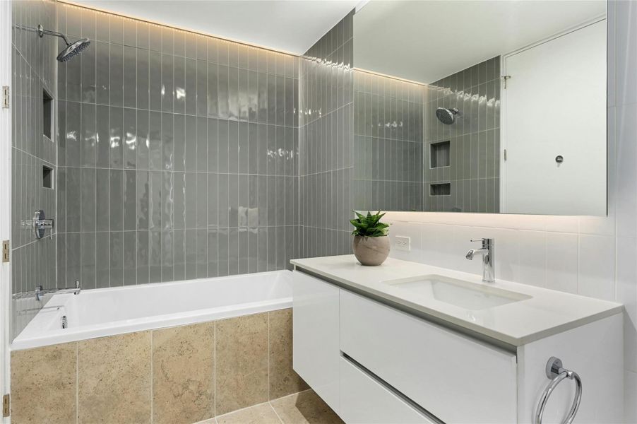 Secondary bathroom with a soaking tub and shower combo, modern vertical tile surround, and a floating vanity with integrated lighting.