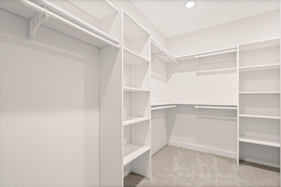 Spacious walk-in closet featuring extensive built-in shelving, multiple hanging rods, recessed ceiling lighting, and light grey carpeting Spacious walk-in closet featuring extensive built-in shelving, multiple hanging rods, recessed ceiling lighting, and light grey carpeting