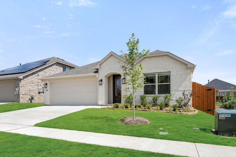 Single-story home with light brick exterior, two-car garage, arched entry, and landscaped front yard with young tree. Single-story home with light brick exterior, two-car garage, arched entry, and landscaped front yard with young tree.