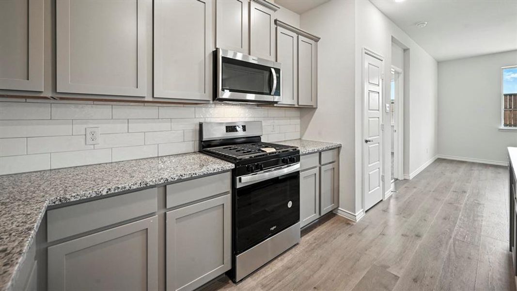 Contemporary kitchen featuring a gas range, built-in microwave, light gray cabinetry, subway tile backsplash, and light-toned countertops