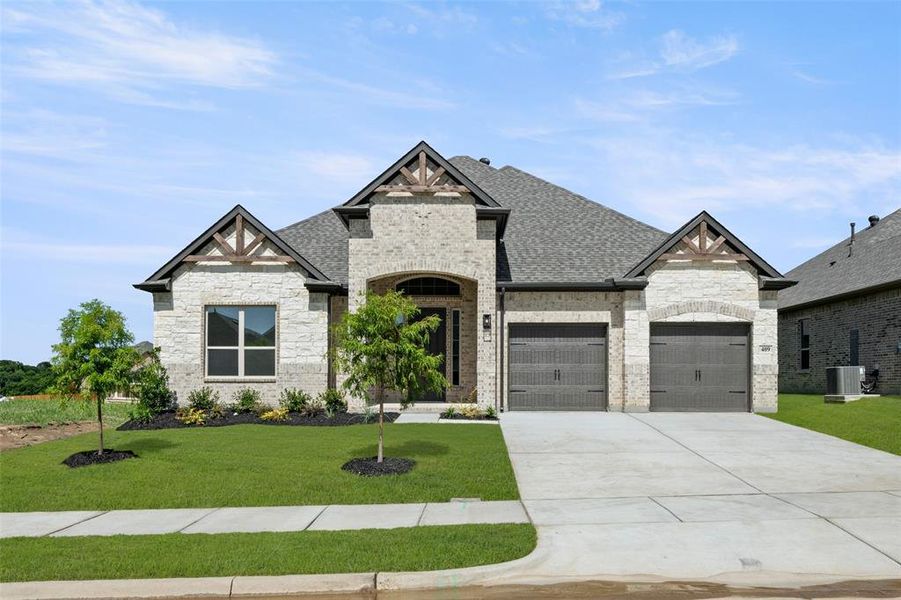 French country home with an attached garage, a front lawn, roof with shingles, concrete driveway, and stone siding French country home with an attached garage, a front lawn, roof with shingles, concrete driveway, and stone siding