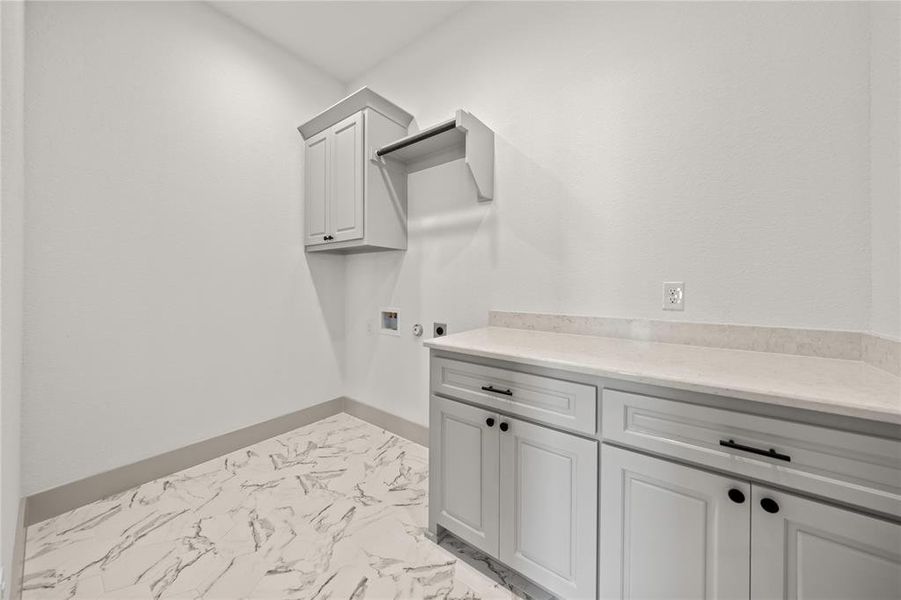 Washroom featuring hookup for an electric dryer, cabinet space, light marble finish floors, and washer hookup Washroom featuring hookup for an electric dryer, cabinet space, light marble finish floors, and washer hookup