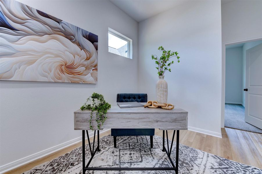 Home office detail showing hardwood floors, clerestory window, high ceilings, and open hallway leading to secondary bedroom.