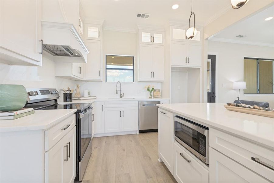 Kitchen featuring white cabinetry, stainless steel appliances, a built-in microwave, light wood-finish flooring, and solid surface countertops