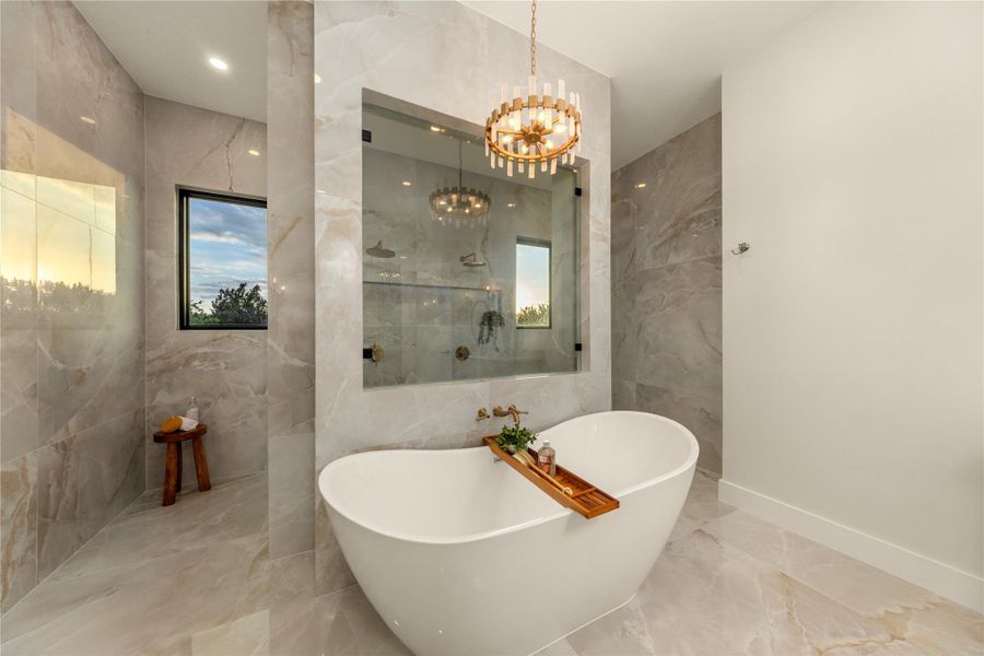 Bathroom with marble tiled floors, tile walls, a freestanding bath, a chandelier, and a marble finish shower