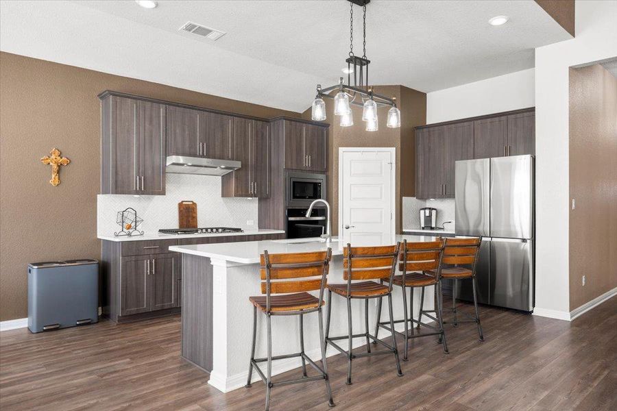 Kitchen with visible vents, appliances with stainless steel finishes, dark brown cabinets, under cabinet range hood, and a sink